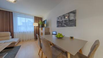 A modern hotel room with a dining area, a sofa, a TV, and a painting on the wall.