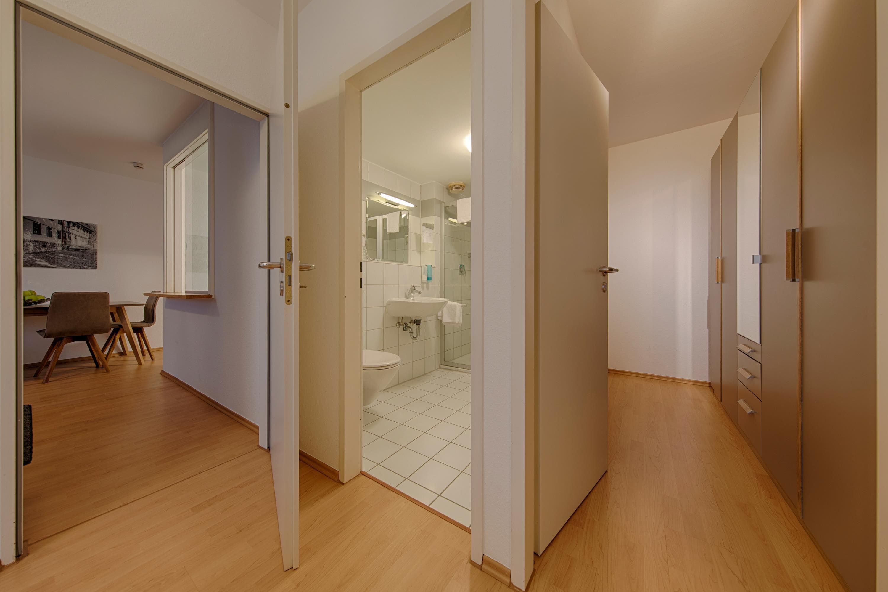 Een modern interieur met een houten vloer, een eethoek met stoelen en een badkamer met toilet en wastafel.