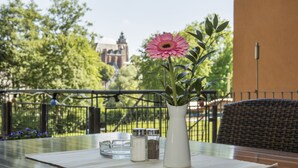 A table with a white vase containing a pink flower, salt and pepper shakers, and a glass. The table is outdoors with a view of a building and trees in the background. - Best Western Hotel Wetzlar (Wetzlar)