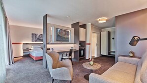 A modern hotel room with a bed, two armchairs, a small table, a desk, a television, and a minibar. - Best Western Hotel Wetzlar (Wetzlar)