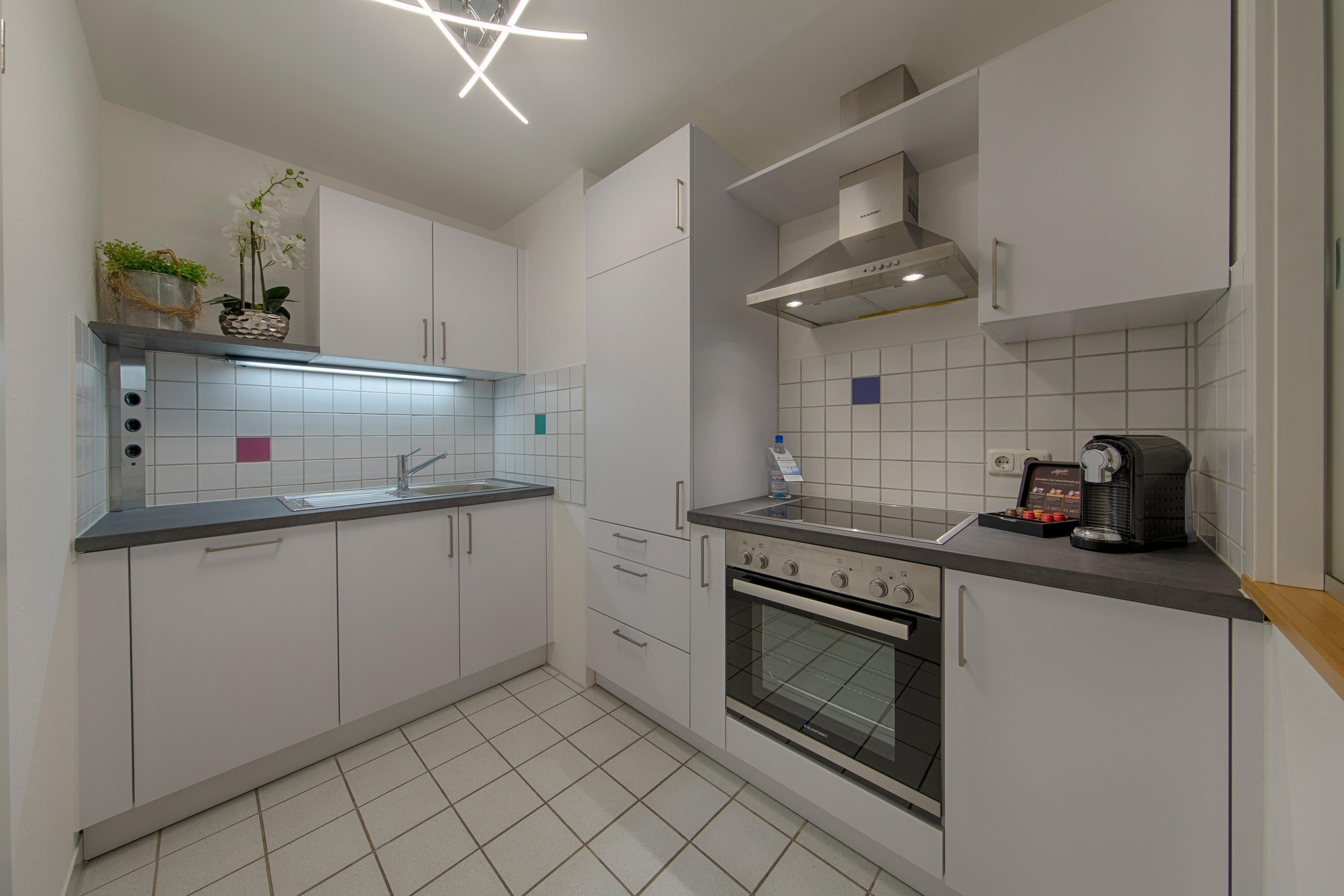 A modern kitchen with white cabinets, a stainless steel range hood, a built-in oven, and a countertop with a coffee machine.