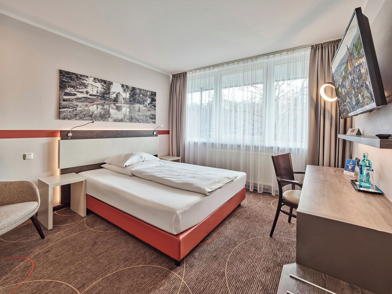 A hotel room with a bed, a desk, a chair, a TV, and a window with curtains.