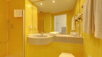A bathroom with yellow tiles, a shower, a sink with a mirror, and towels.