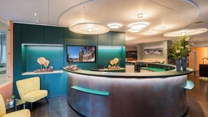 A reception area with a curved desk, teal walls, and a large window. There are yellow chairs and a vase of flowers. - Best Western Hotel Wetzlar (Wetzlar)