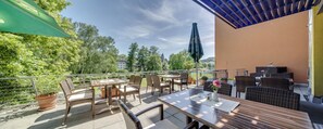 An outdoor patio with wicker furniture, a table with a vase of flowers, and a view of trees and buildings in the background. - Best Western Hotel Wetzlar (Wetzlar)