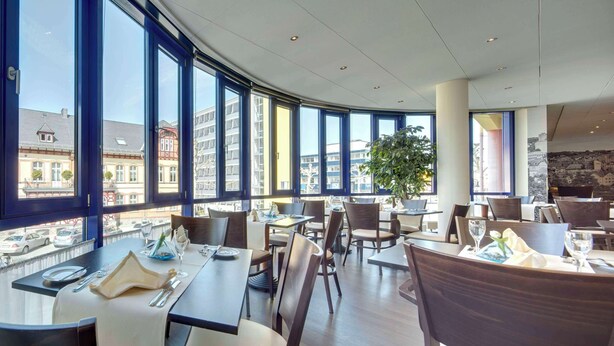 A modern dining area with large windows, a view of buildings, and a plant. - Best Western Hotel Wetzlar (Wetzlar)