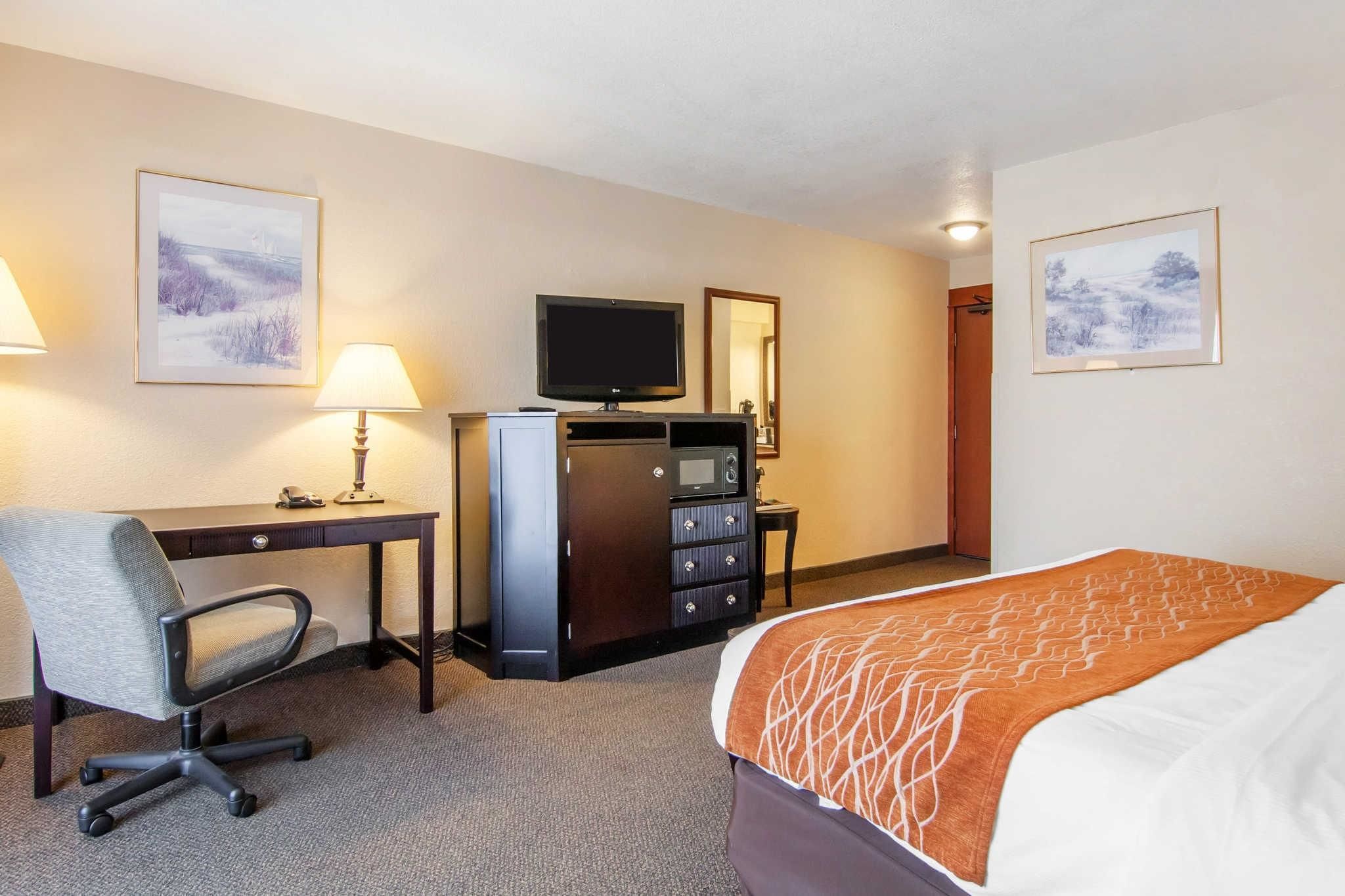 A hotel room with a bed, desk, chair, TV, dresser, and two framed pictures on the walls.