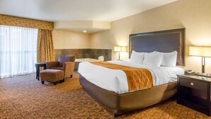 A hotel room with a large bed, a chair, a small table, and a lamp.