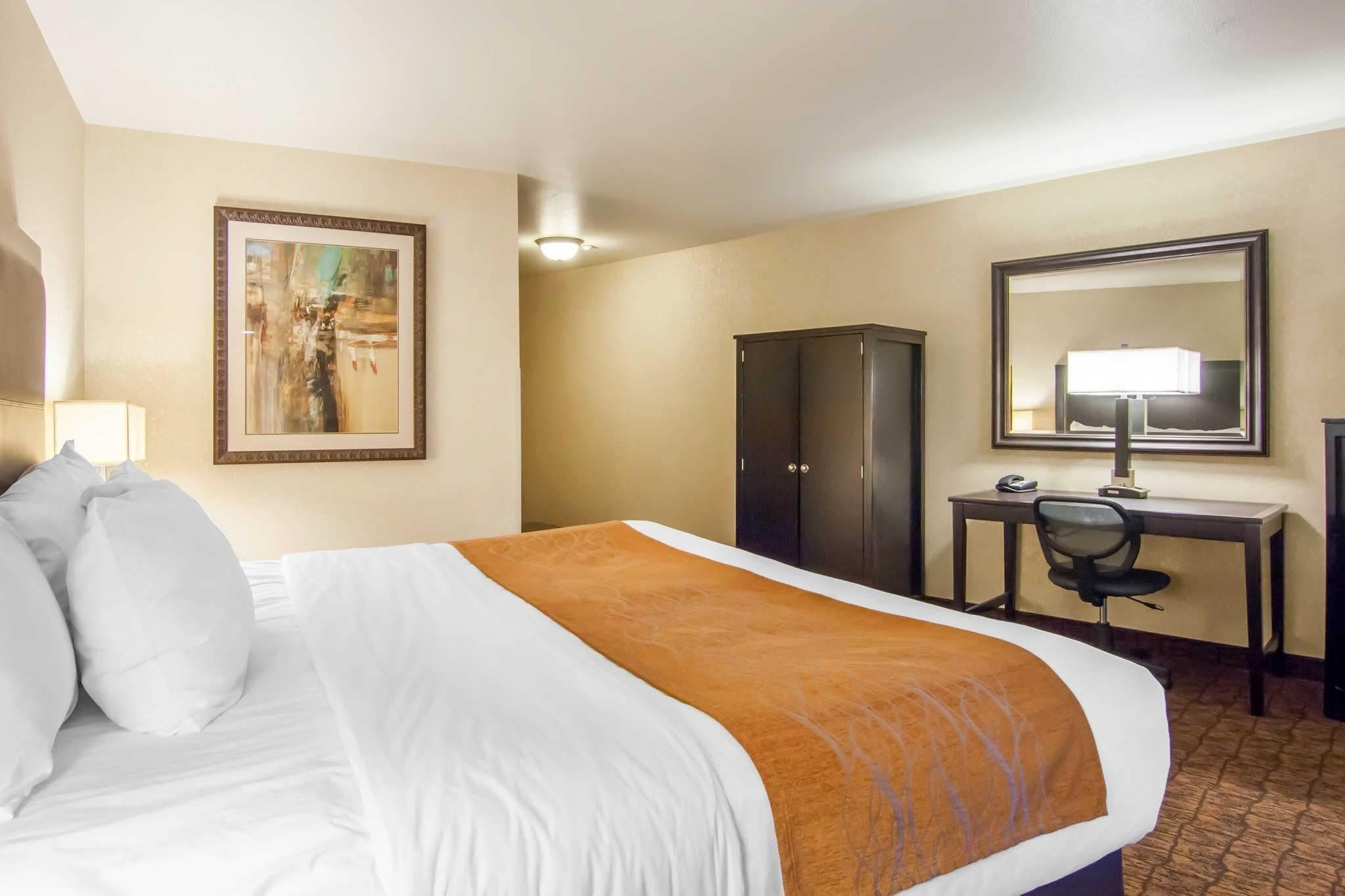 Une chambre d’hôtel avec un grand lit, un bureau, une chaise, une armoire et un tableau au mur.