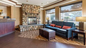 A lobby with a stone fireplace, a blue sofa with red cushions, a wooden reception desk, and a large window offering a view of trees.