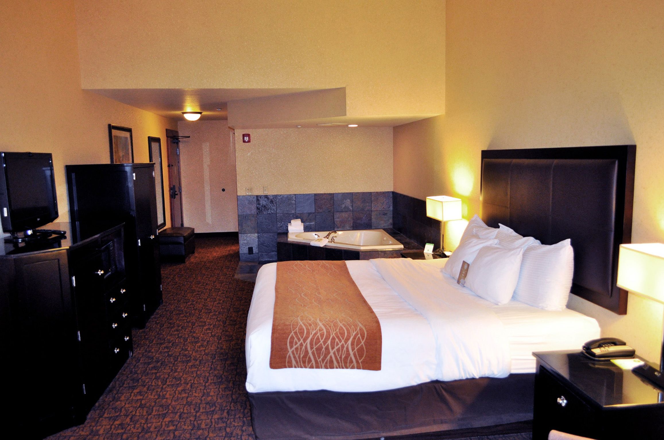 A hotel room with a large bed, a desk with a lamp, a television, and a bathroom with a bathtub.