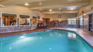 An indoor swimming pool with clear water, stone walls, and a clock on the wall.