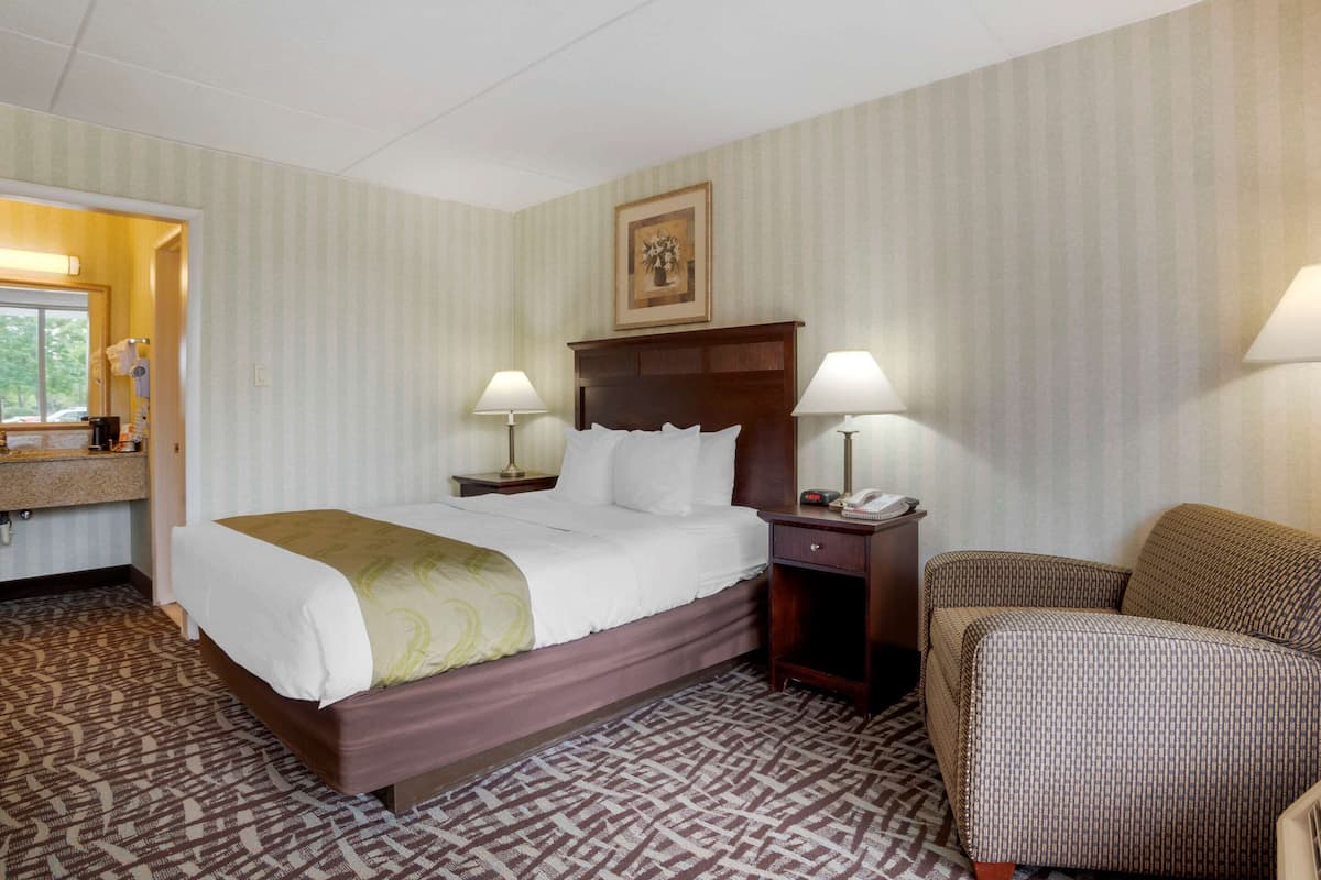 Ein Hotelzimmer mit einem großen Bett, zwei Nachttischen mit Lampen, einem Sessel und einem gemusterten Teppich.