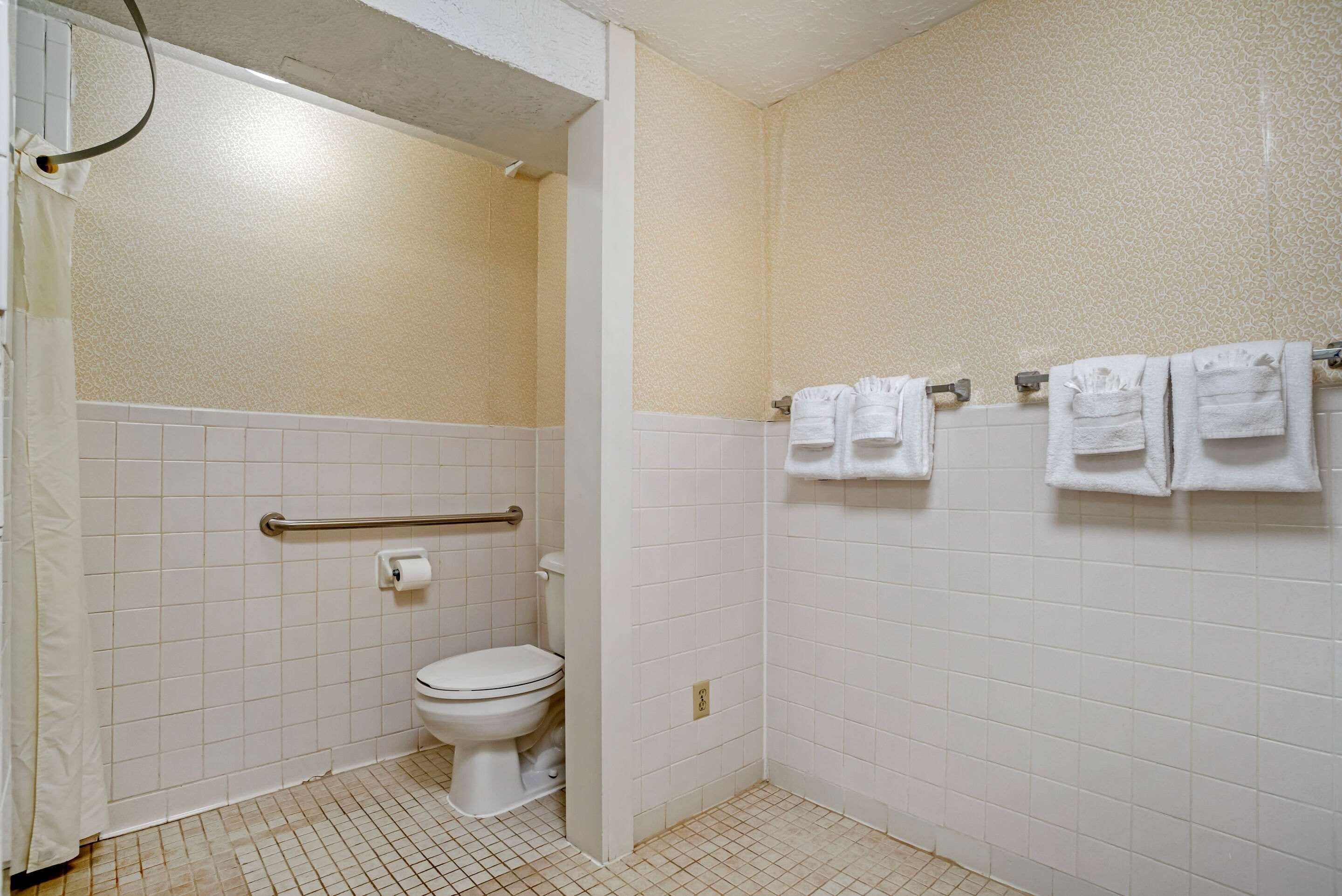 A small, clean bathroom with a toilet, a shower area, and a towel rack with several towels.