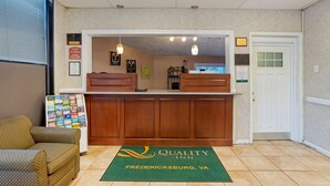 A reception area with a wooden counter, a green carpet with the hotel name, and a door to the right.
