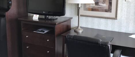 Une chambre d’hôtel équipée d’un bureau, d’une télévision, d’une lampe, d’un tableau encadré et d’une moquette à motifs.