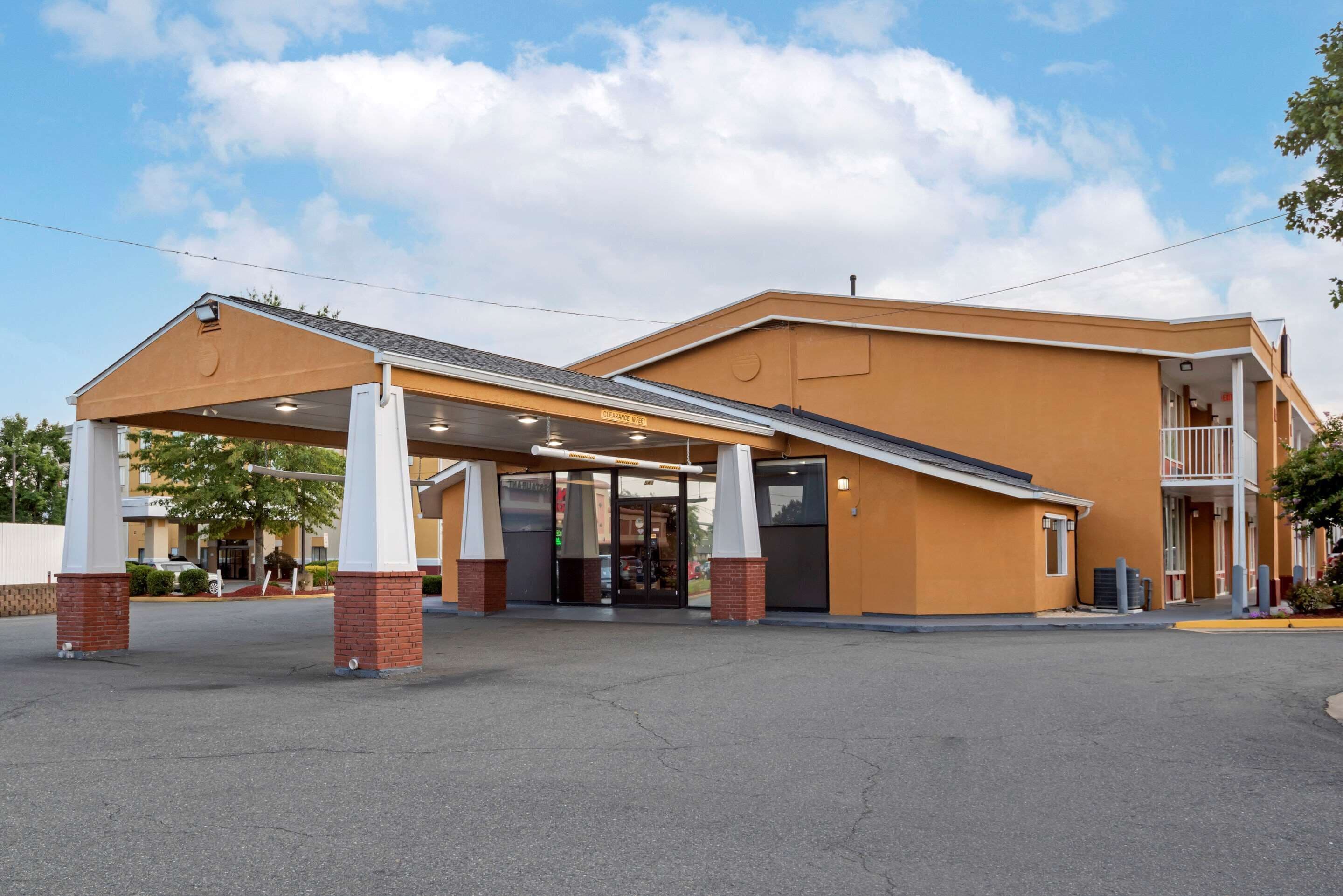 A hotel with a covered entrance, a balcony, and a parking lot.