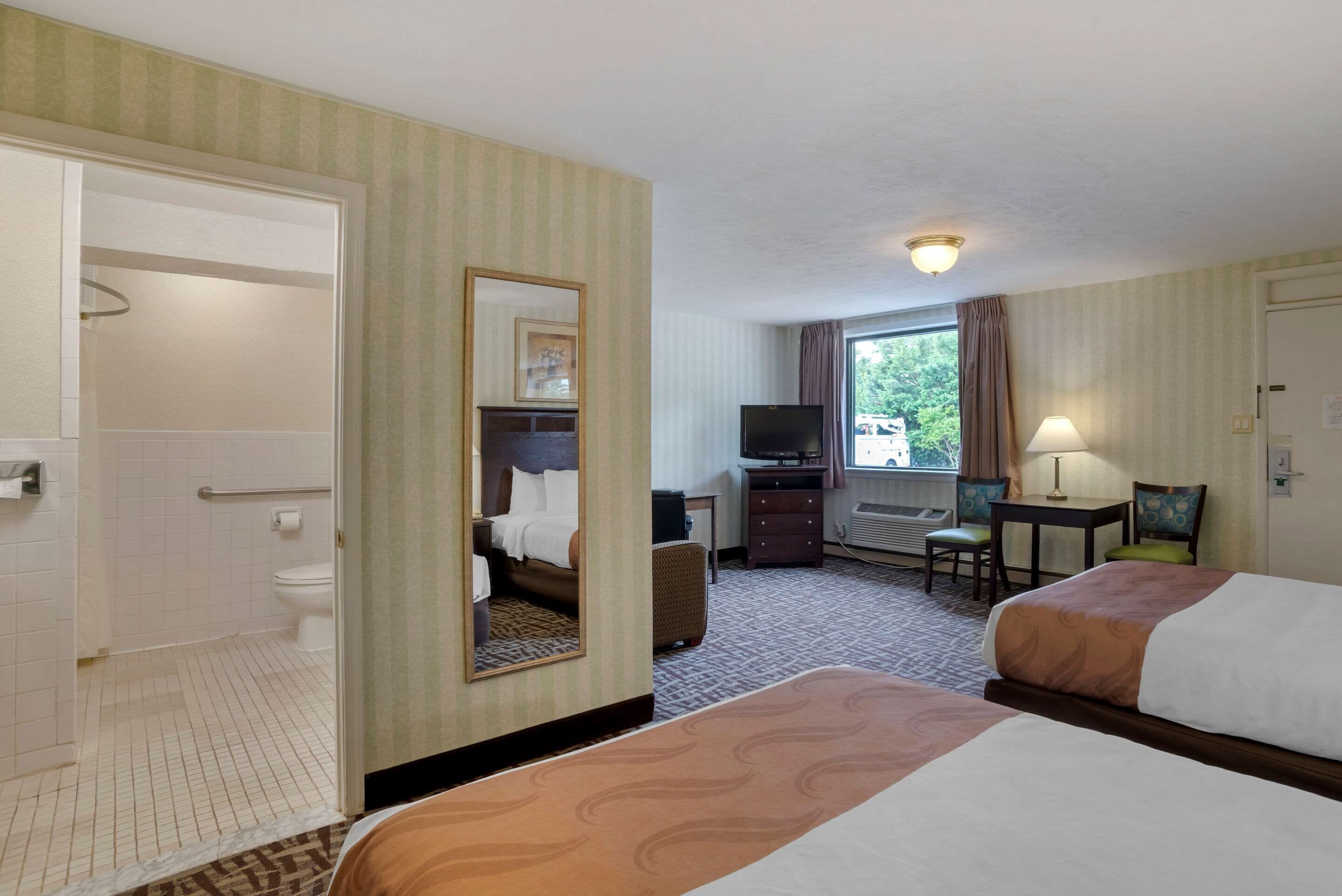 A hotel room with two beds, a bathroom, a desk with a chair, a television, and a window with curtains.