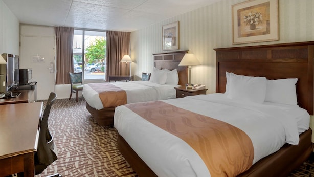 A hotel room with two beds, a desk, a chair, a TV, and a window with curtains.