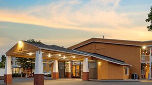 A hotel entrance with a covered walkway, a sign indicating the name, and a clear sky.