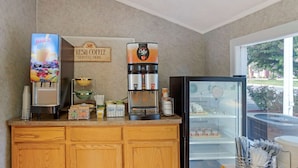 A coffee station with a juice dispenser, a coffee machine, and a refrigerator stocked with beverages.