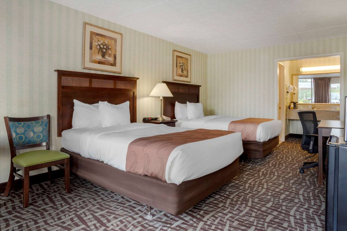 Ein Hotelzimmer mit zwei Betten, einem Schreibtisch, einem Stuhl und einem Spiegel.