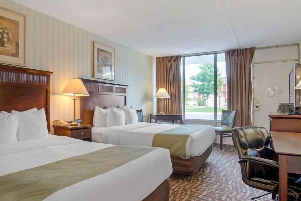 Ein Hotelzimmer mit zwei Betten, einem Schreibtisch, Stühlen und Blick ins Freie.
