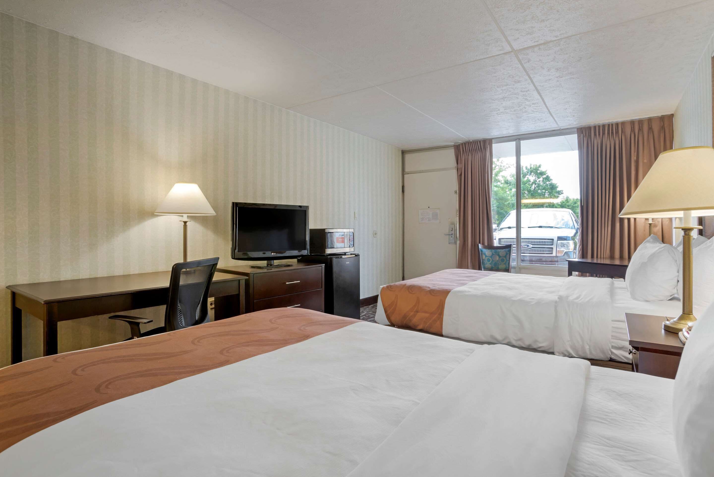 Habitación de hotel con dos camas, un escritorio, un televisor y una ventana con cortinas.