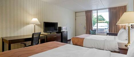 Habitación de hotel con dos camas, un escritorio, un televisor y una ventana con cortinas.