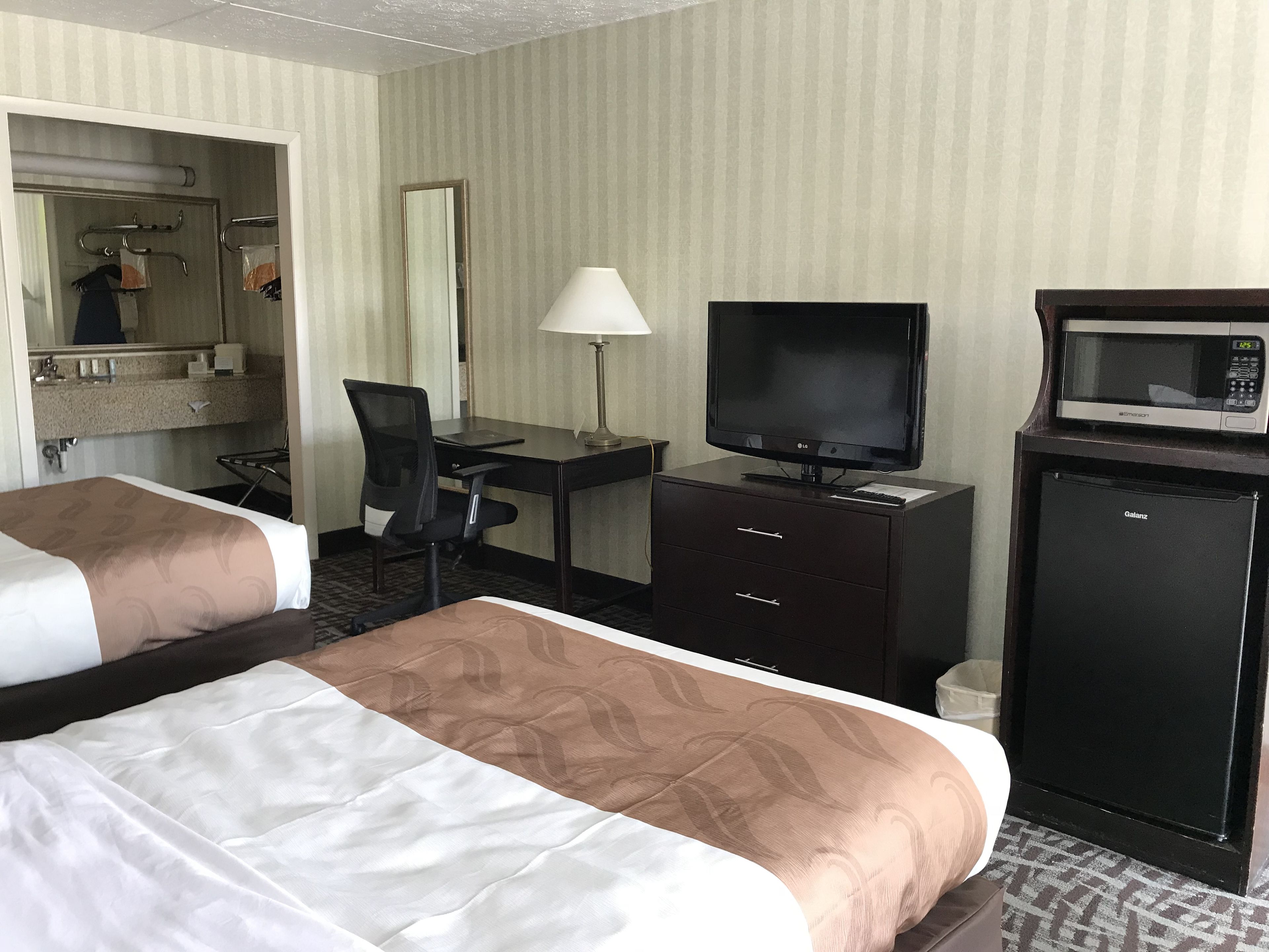 Habitación de hotel con dos camas, un escritorio con computadora, televisión, microondas y refrigerador pequeño.