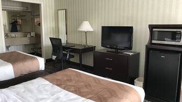 Habitación de hotel con dos camas, un escritorio con computadora, televisión, microondas y refrigerador pequeño.