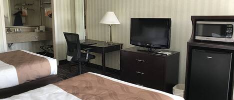 Habitación de hotel con dos camas, un escritorio con computadora, televisión, microondas y refrigerador pequeño.