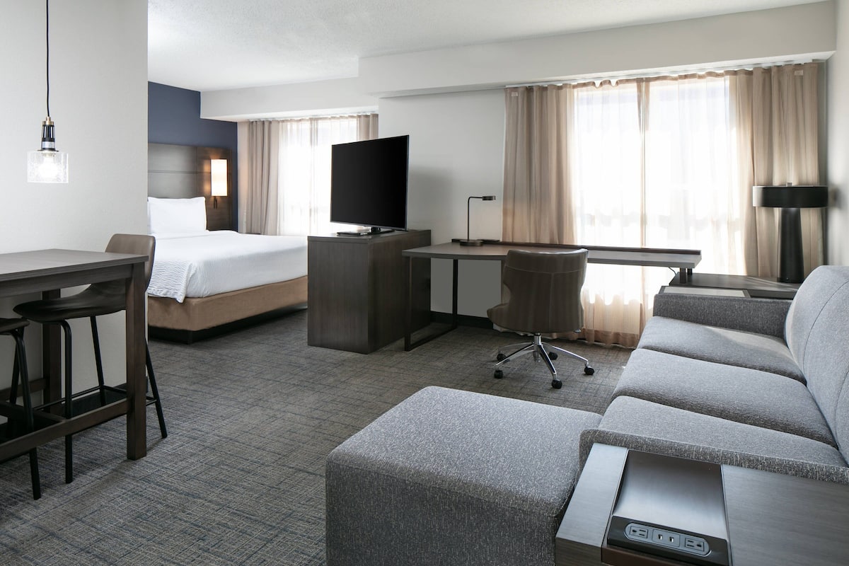 A hotel room with a bed, a desk, a television, a sofa, and a bar area.