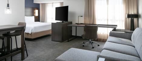 A hotel room with a bed, a desk, a television, a sofa, and a bar area.