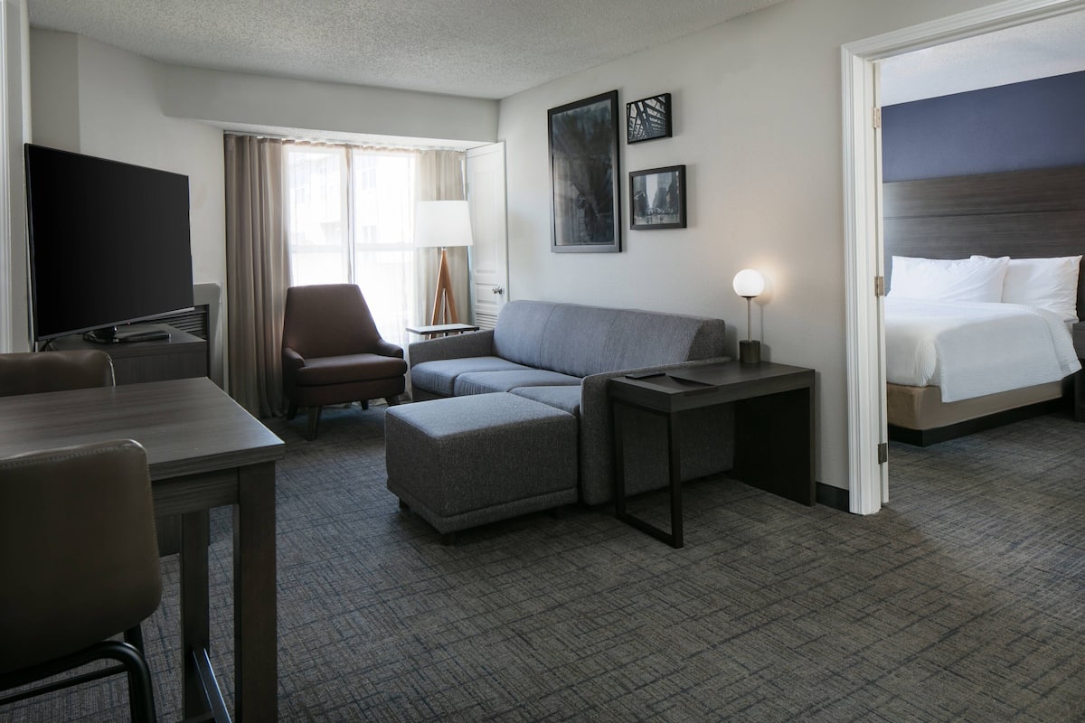 A hotel room with a bed, a sofa, a desk, a TV, and a lamp.