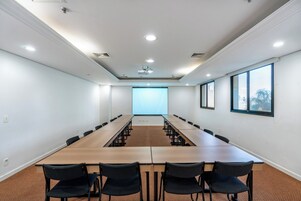 A conference room with a long table, chairs, a projector screen, and windows.