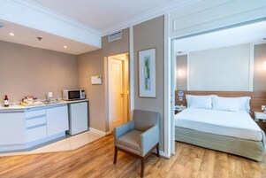 Habitación de hotel con cama, una silla, kitchenette y una puerta que conduce a otra habitación.
