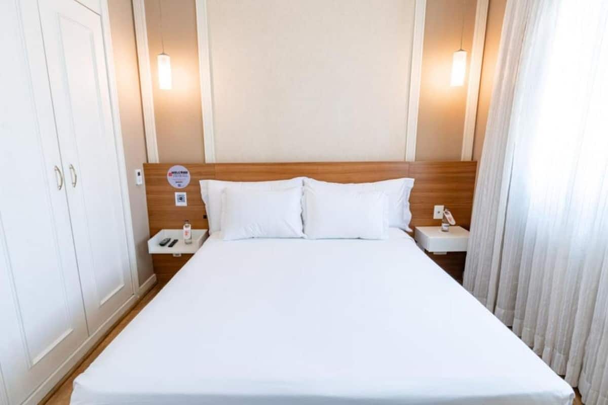 Una camera d'albergo con un letto grande, due comodini, un armadio e una lampada a parete.