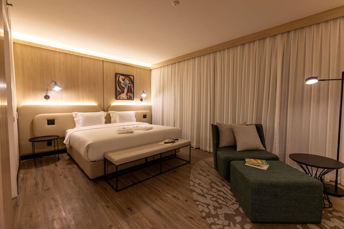 Una camera d'albergo con un letto, comodini, una poltrona, una sedia da lettura e un piccolo tavolino.