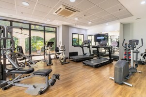 A gym with cardio machines, weight machines, and a television screen.