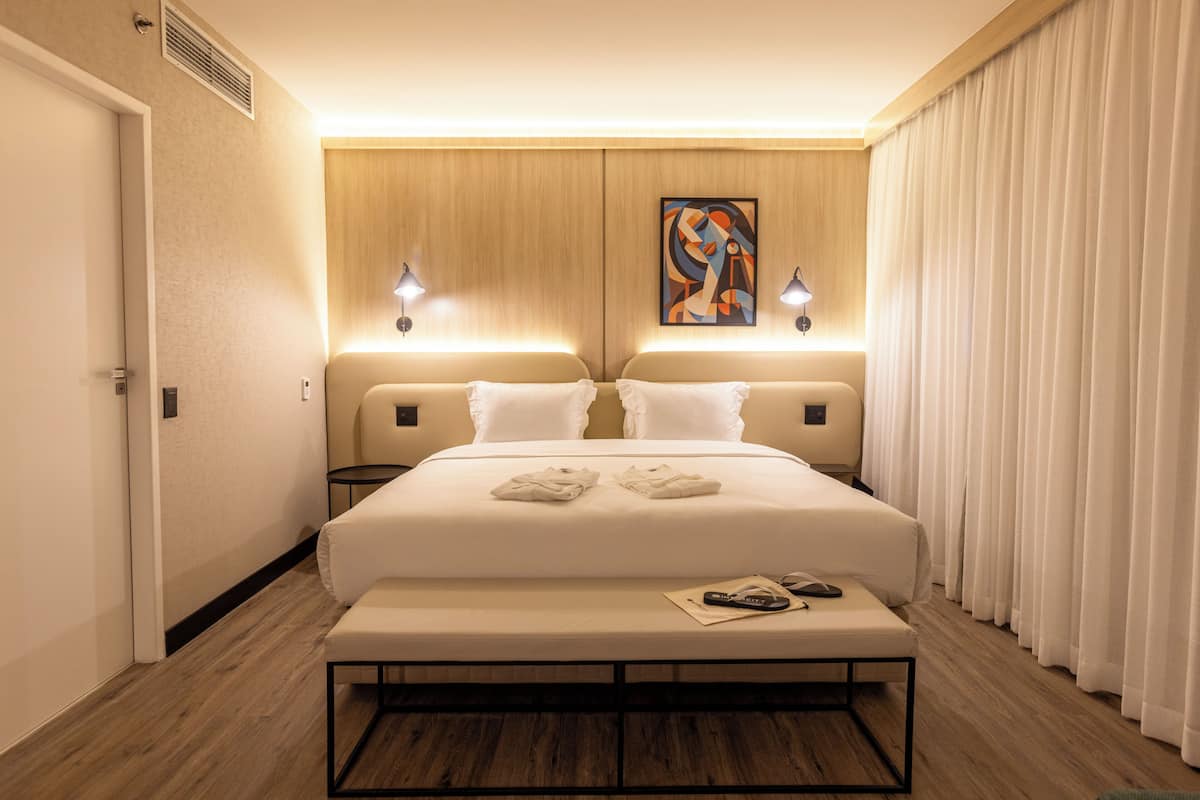 Camera d'albergo con un letto grande, due comodini, una panca ai piedi del letto e un quadro appeso al muro.