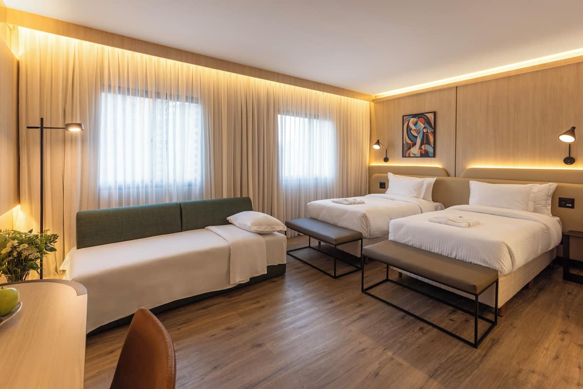 Una camera d'albergo con due letti, un divano, una panca, una scrivania e una lampada.