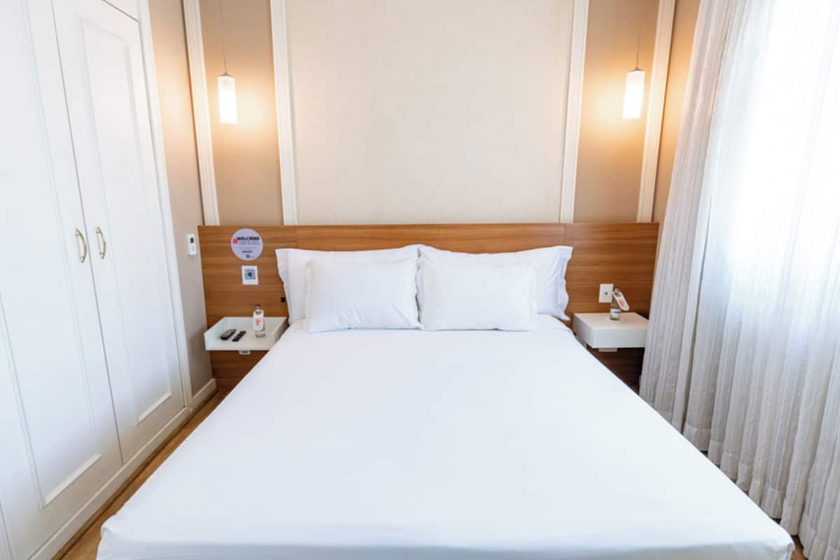 Camera d'albergo con un letto grande, una testiera in legno, comodini con lampade e una porta con maniglia.