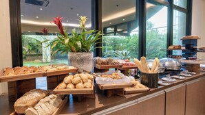 A buffet counter with various baked goods and pastries, a potted plant, and a view of greenery outside. - Intercity Pamplona - The Universe Paulista (São Paulo)
