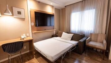 Ein Hotelzimmer mit Bett, Schreibtisch, Stuhl, Fernseher und einem Fenster mit Vorhängen.