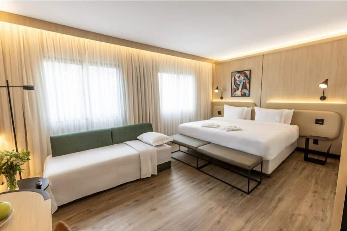 Una camera d'albergo moderna con un letto, un divano, una panca e una scrivania.