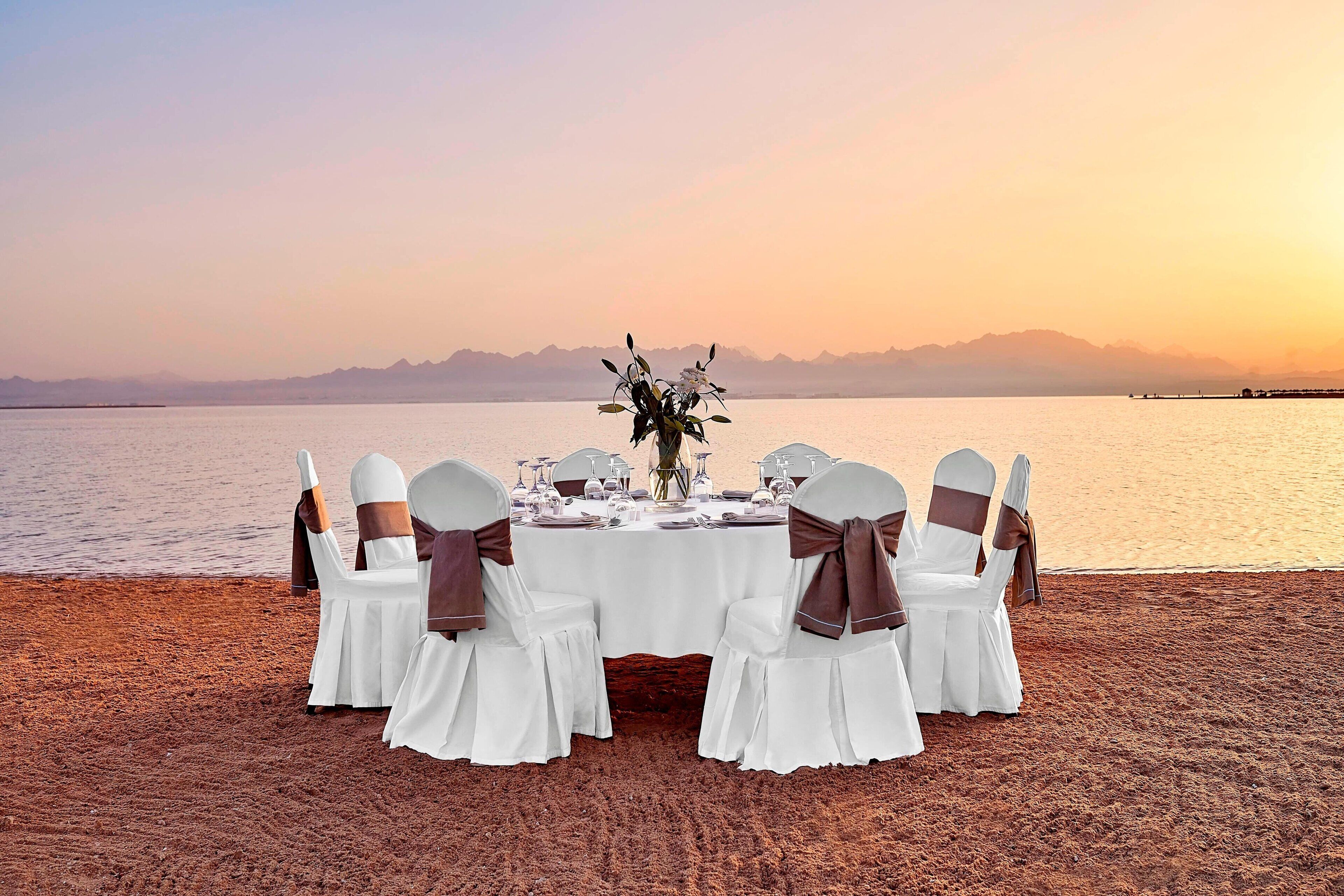 A table set for a meal on a beach with a view of mountains in the background.