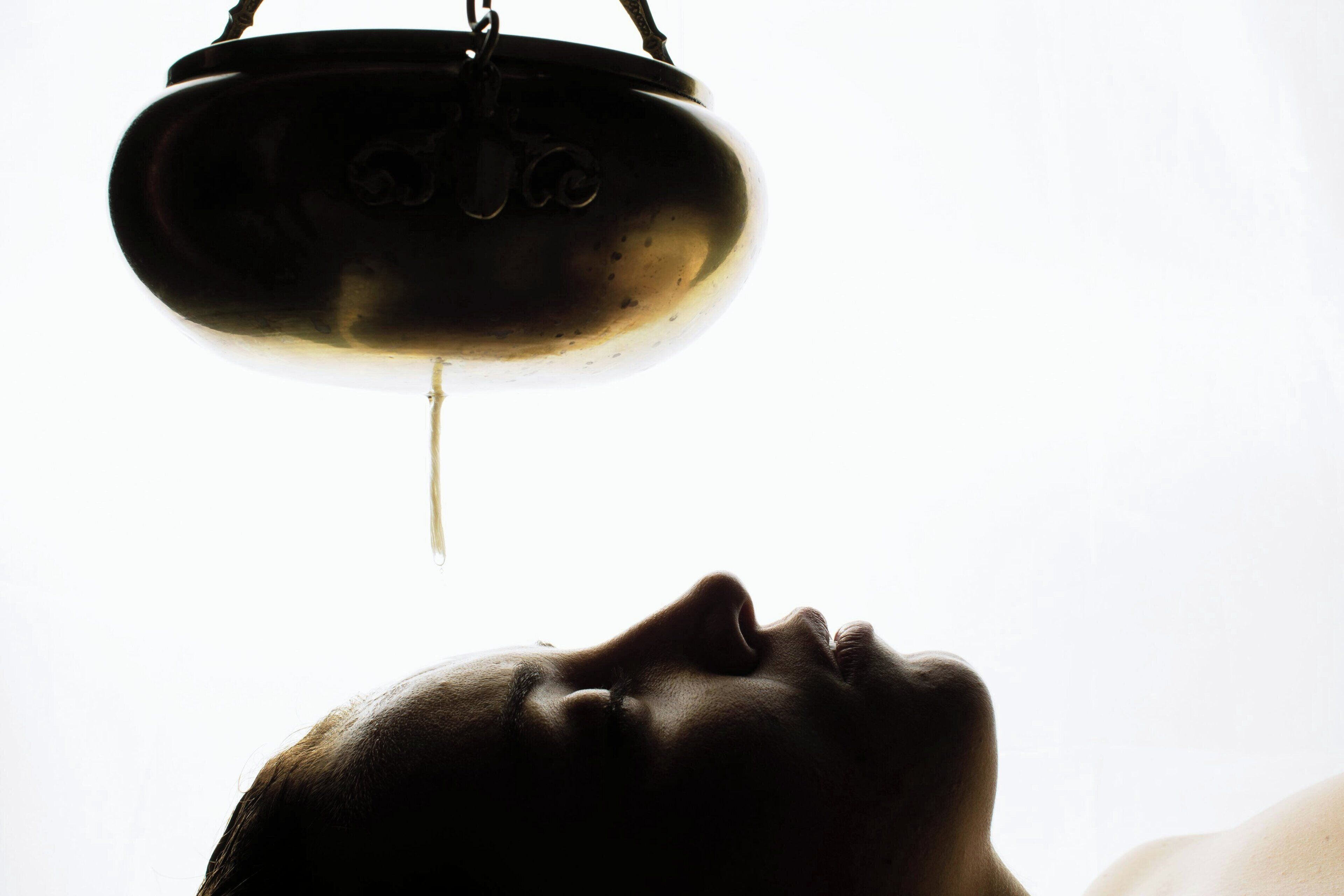 A person with their head tilted upwards, looking at a hanging object that appears to be a pot or container with a liquid dripping from it.