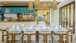 A dining area with a long table set for a meal, wooden chairs, and a kitchen in the background. - Sheraton Soma Bay Resort (Soma Bay)