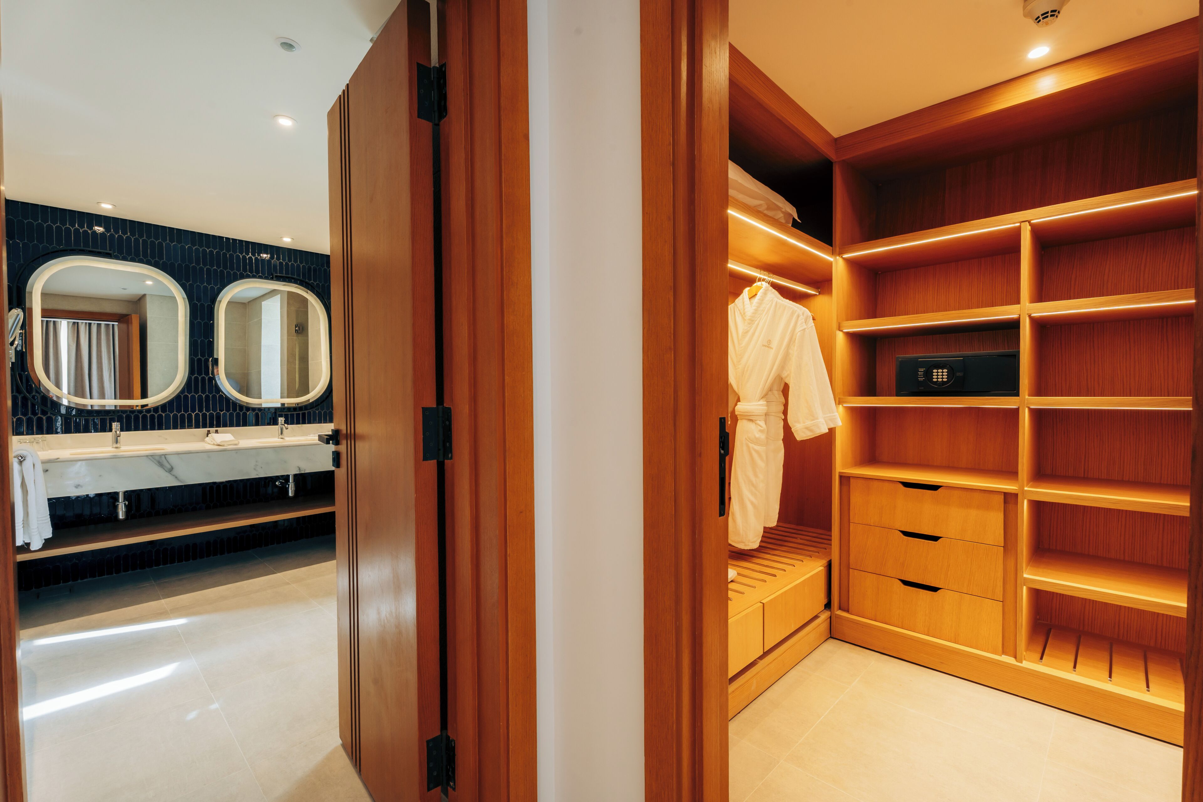 Ein modernes Badezimmer mit Waschtisch, zwei Spiegeln und einem begehbaren Kleiderschrank mit Holzböden und einem Bademantel.